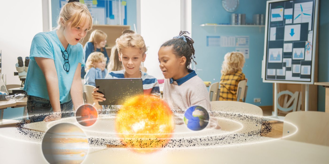 Crianças em sala de aula usam um tablet para descobrir o sistema solar. O Sol e alguns planetas se materializam diante deles.