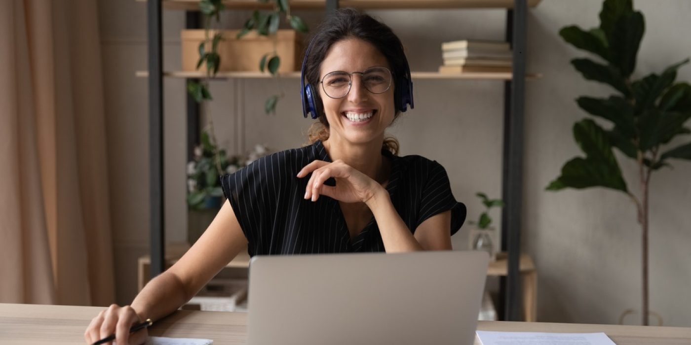 jovem professora está sentada usando o notebook estudando e sorrindo para a câmera