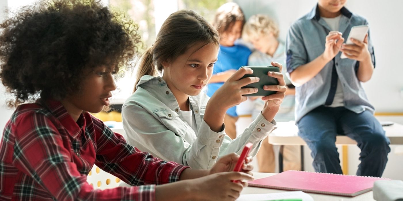 Jovens estudantes usando celular na sala de aula, individualmente.