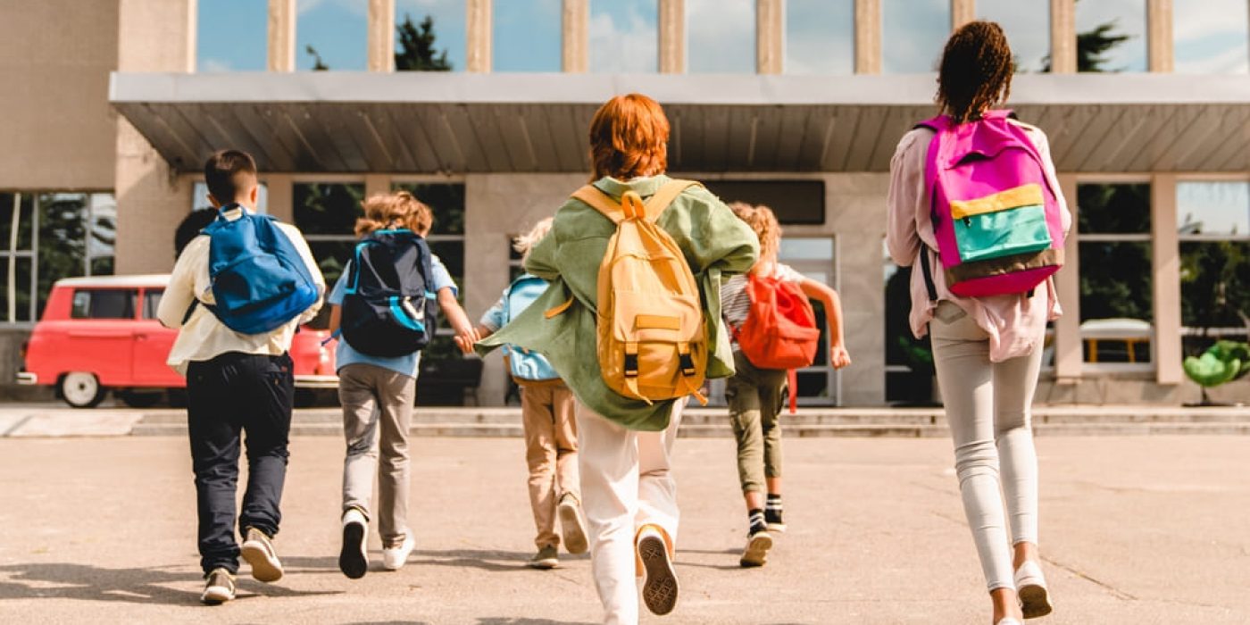 Crianças chegando à escola com mochilas, simbolizando aumento de matrículas após estratégias de captação de alunos.