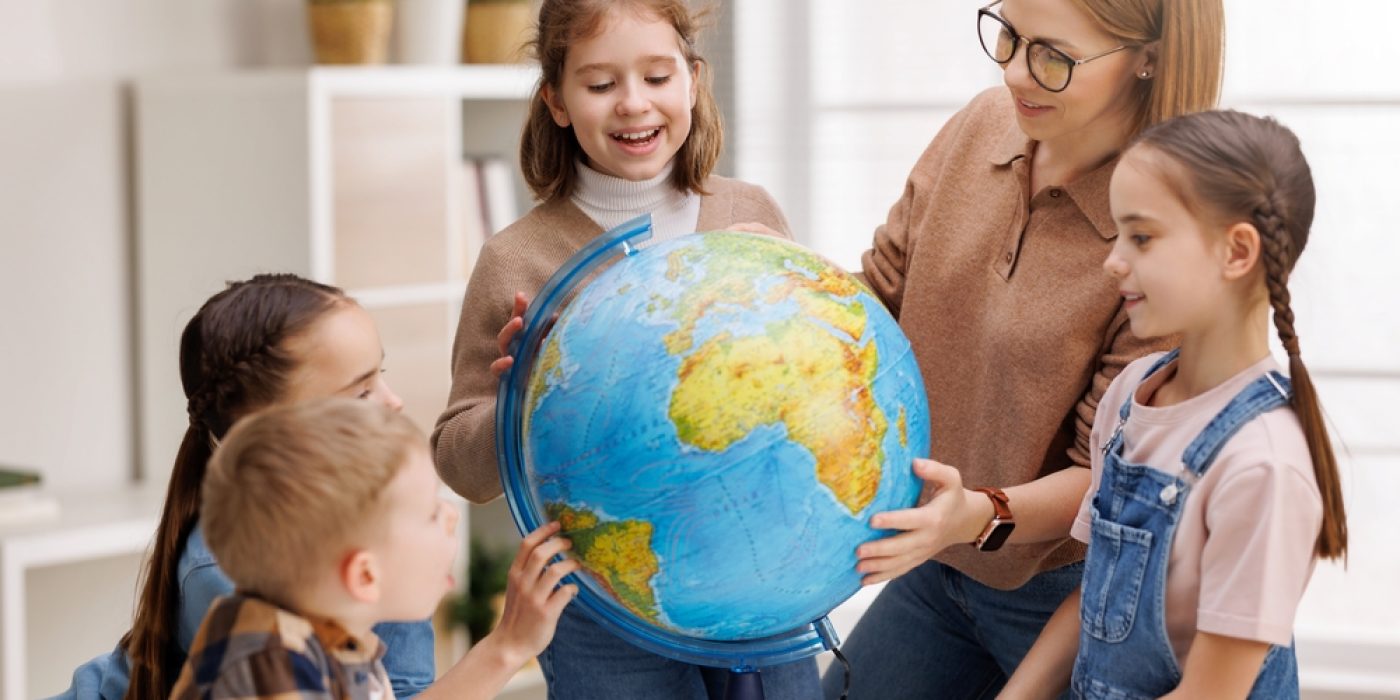 Professora com crianças ao redor de um globo do planeta Terra.