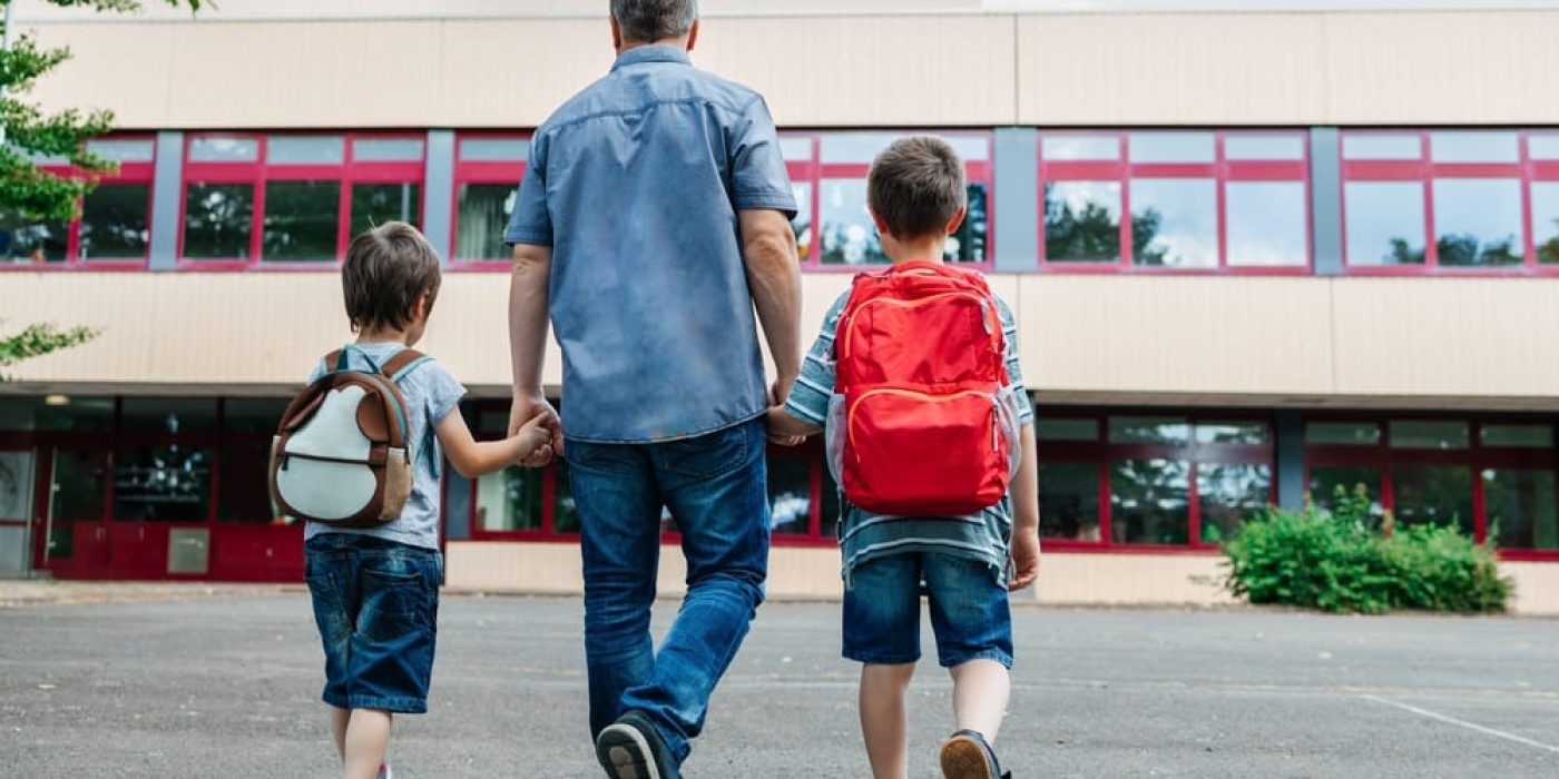 Pai levando seus filhos para o colégio, representando a integração entre família e escola, fator importante na realização de atividades lúdicas sobre família na Educação Infantil.