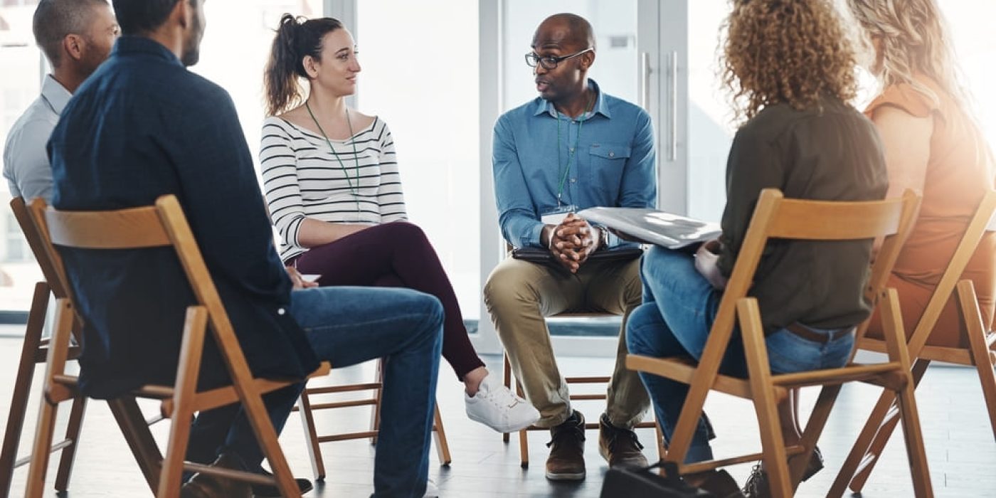 Dinâmica para reunião de pais com seis adultos sentados em círculo, discutindo em um ambiente claro e iluminado.