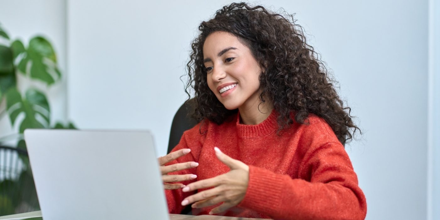 Mulher participando de aula híbrida, comunicando-se em frente a um notebook.