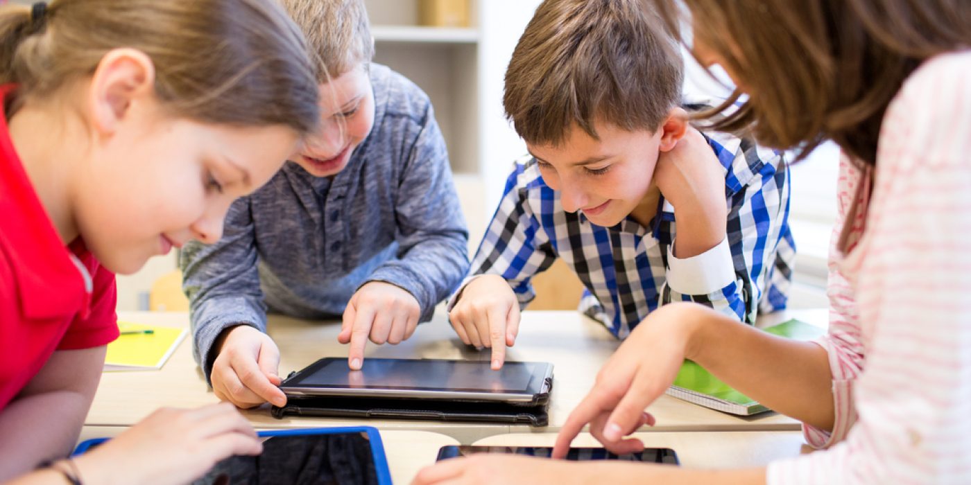 Crianças usam tablets ao redor de uma mesa na escola