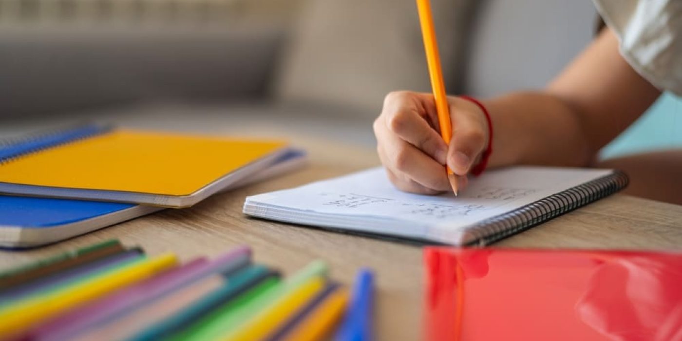 Criança escrevendo em caderno durante atividade de aprendizagem, um dos tipos de avaliação segundo a BNCC.