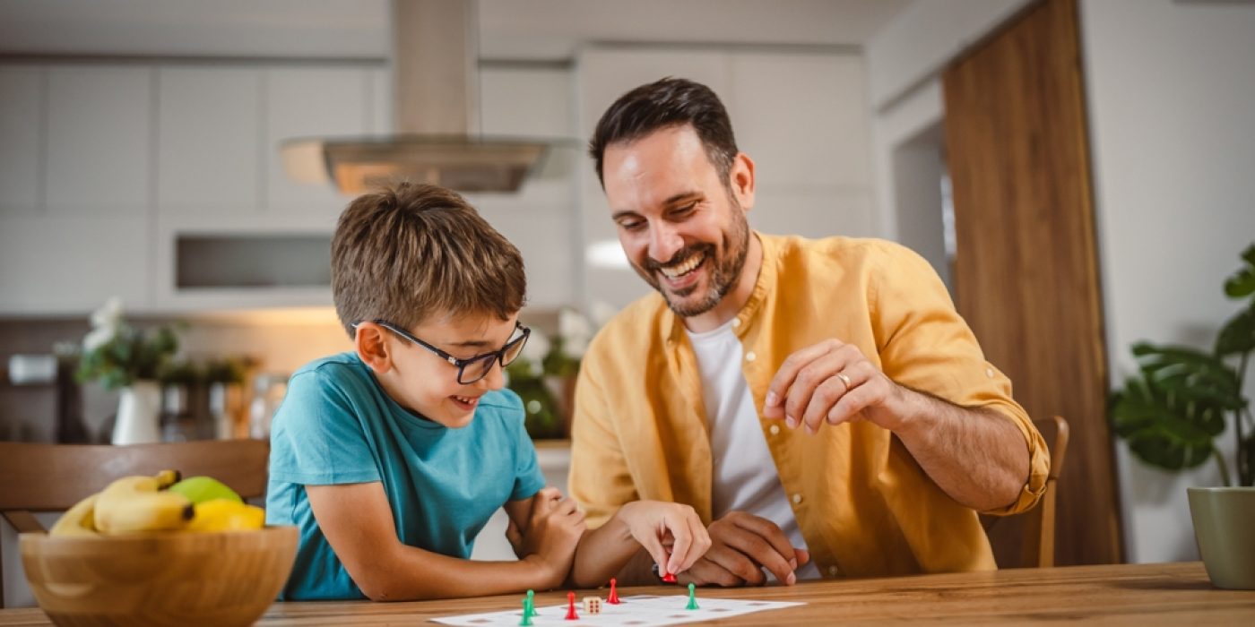 Pai e filho se divertem com um jogo de tabuleiro em casa.