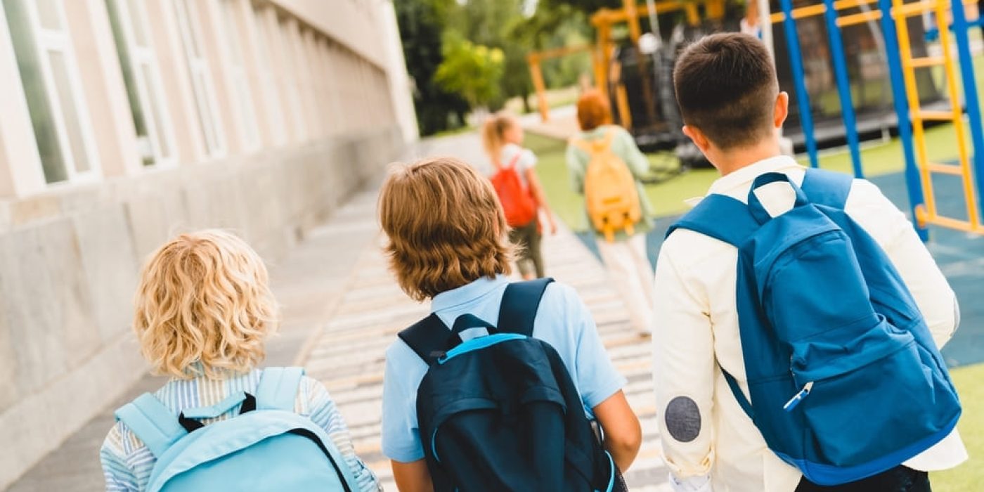 Crianças caminhando com mochilas para escola no primeiro dia de aula.