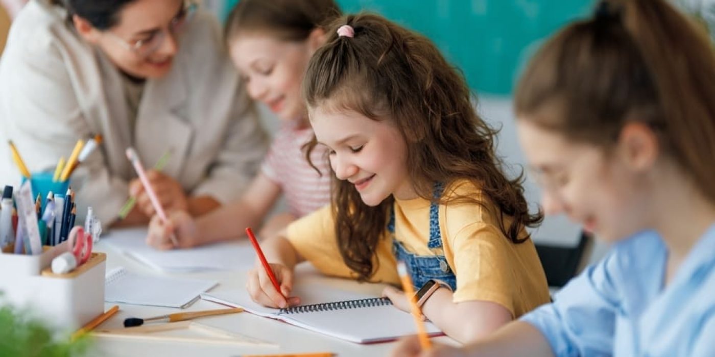 Professora e crianças interagindo em sala de aula, com foco no aprendizado de inglês. A imagem ilustra a importância de começar cedo o aprendizado de idiomas.
