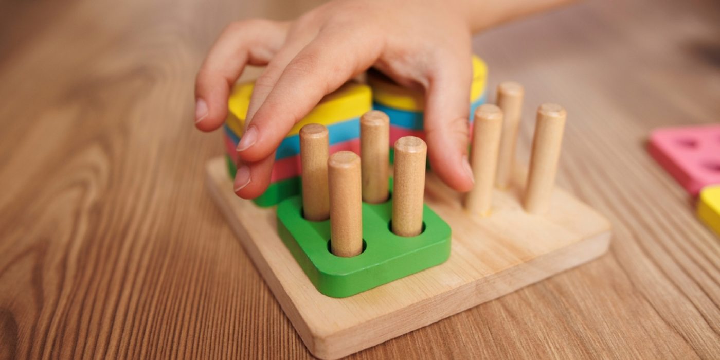 Mão de criança segurando e brincando com um brinquedo, representando a rotina da educação infantil.