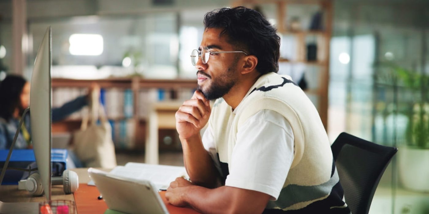 Homem estudando inglês em seu computador com livros, focado na leitura e compreensão de textos.