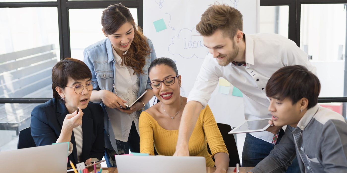 Equipe reunida em frente ao computador trabalhando de forma colaborativa, exemplo da gestão democrática da escola.